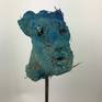 Scultura astratta di volto dipinto con pigmenti blu. L'opera è realizzata in terra cruda con paglia, sabbia, segatura, legno e altre fibre vegetali. Questo lavoro vuole rappresentare il gesto primitivo del creare con elementi naturali sempre esistiti.