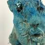 Scultura astratta di volto dipinto con pigmenti blu. L'opera è realizzata in terra cruda con paglia, sabbia, segatura, legno e altre fibre vegetali. Questo lavoro vuole rappresentare il gesto primitivo del creare con elementi naturali sempre esistiti.