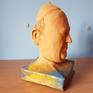 E' una scultura in terracotta.
E' rappresentato il ritratto di papa Francesco poggiato su un libro.
La testa non è a tuttotondo ma è rappresentato solo la parte anteriore.
Il volto è realistico, ma la composizione nell'insieme è surrealista.