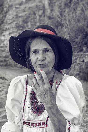 An old woman, a grandmother with long hair in a white dress and hat, sits on the shore and gesticulates something. thumb