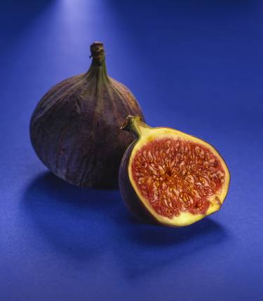A halved and whole fig isolated on a blue background thumb