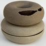 A small sculpture, composed of two parts, the bottom gray and the upper brown.
Both have a circular shape with a hole in the center (like a pretzel) and a destruction of the shape that allows a peek inside.
The parts are not connected so their posture can be changed