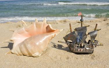 Big shell and little toy sailing ship on beach thumb