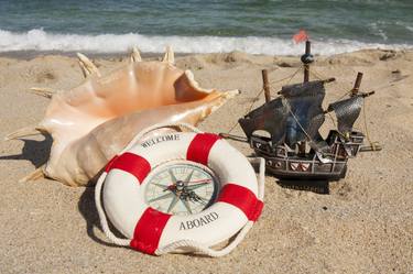 Big shell, toy sailship and life preserver on sandy beach thumb