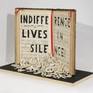 "Indifference lives in...silence!" is carved on an old music sheet. The single letter fallen in front of the book.