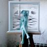 a ceramic sculpture in awoden frame symbolizing the sea view iconized in atransparent plexiglass panel.the female nude is posing with grace as if in front of a mirror ant the sea horizon behind her indicates the waiting of a journey to begin..