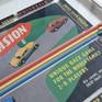A vintage board game box and acrylic painted wood on canvas with a three-dimensional element. The work is mounted behind glass within a white, wooden frame.

Featuring a rare British board game from the 1950’s, this box has been deconstructed and dissected with strips of painted wood that match the colors of the hand-drawn cars. 

The direction of the wooden strips is intended to oppose the driving direction of the vehicles and the arrow-like wooden corners echo the arrowed Diversion sign.
